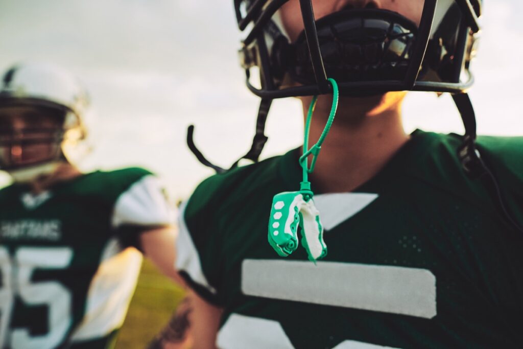 Closeup of a young American football player with his mouthguard hanging from his helmet during an afternoon practice